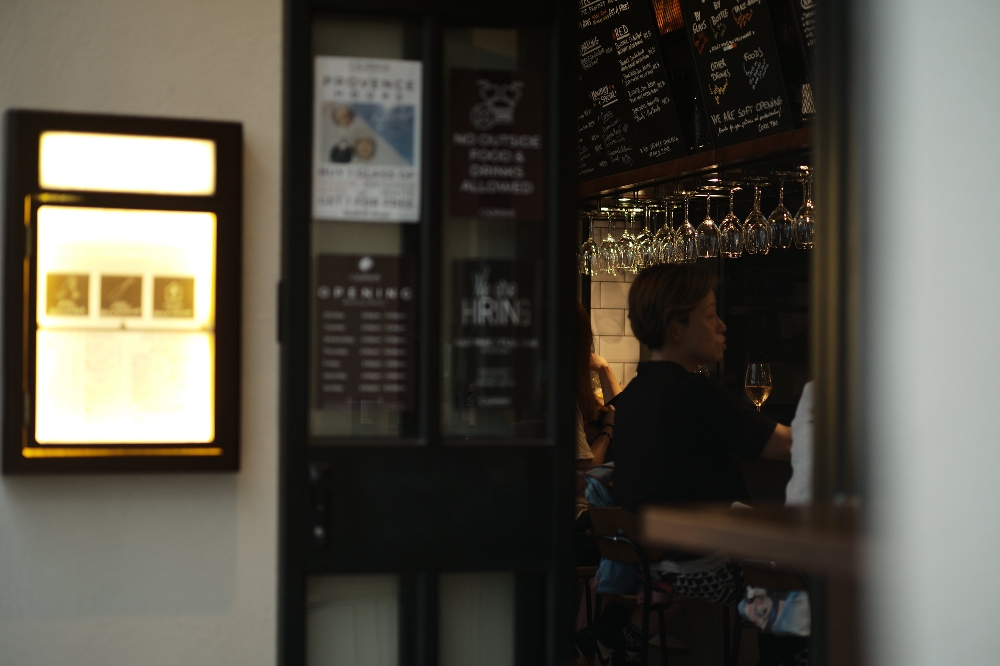 Photo sample from a Leica ELCAN 66mm f/2 — evening wine bar in Hong Kong seen through a doorway, wine glasses hanging above the counter