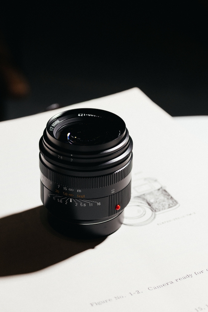 Leica Summicron-M 66mm f/2 limited edition in black anodized finish, standing on a KE-7A manual page in hard sunlight